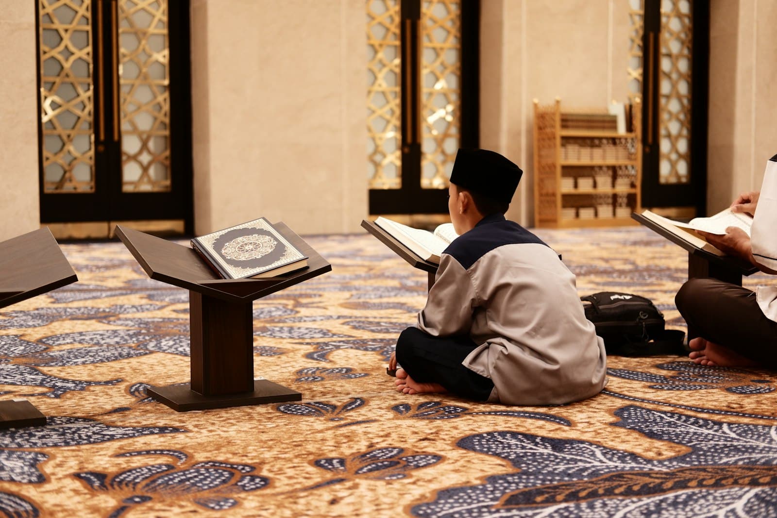 A boy reciting from a Quran on a wooden stand inside a mosque