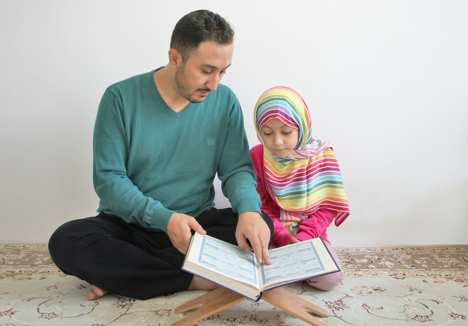 A father and his young daughter reading the Quran together on a wooden stand