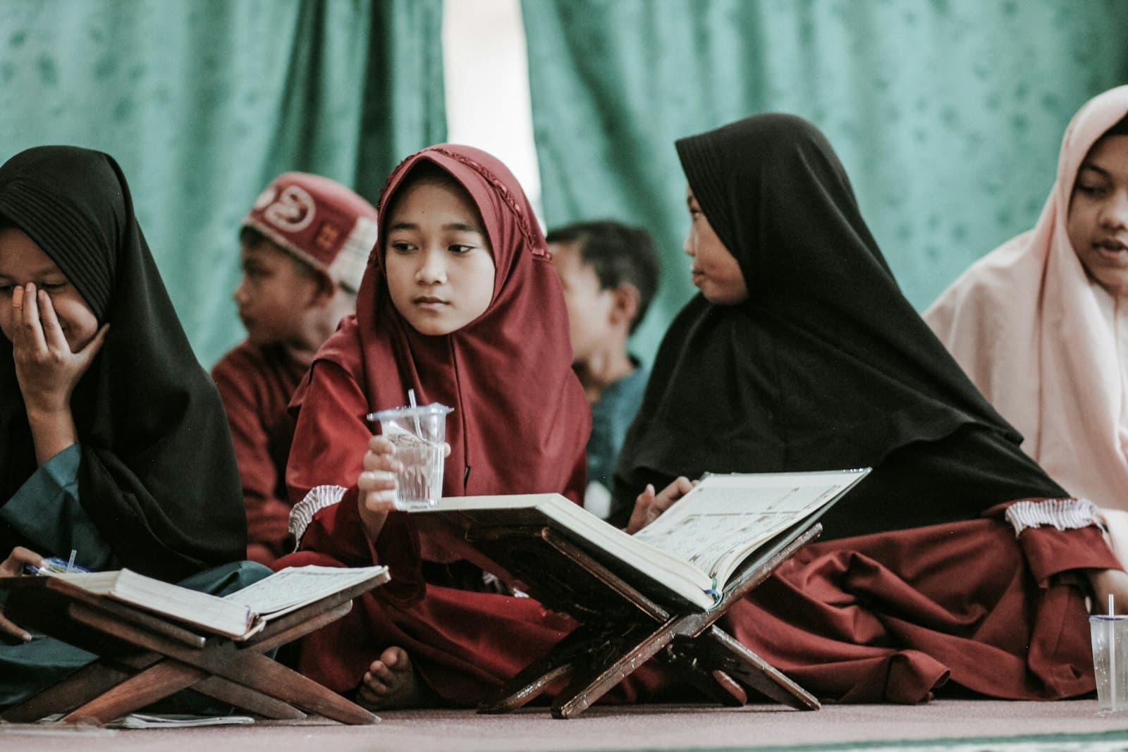 Girls in hijab reading the Quran on wooden stands