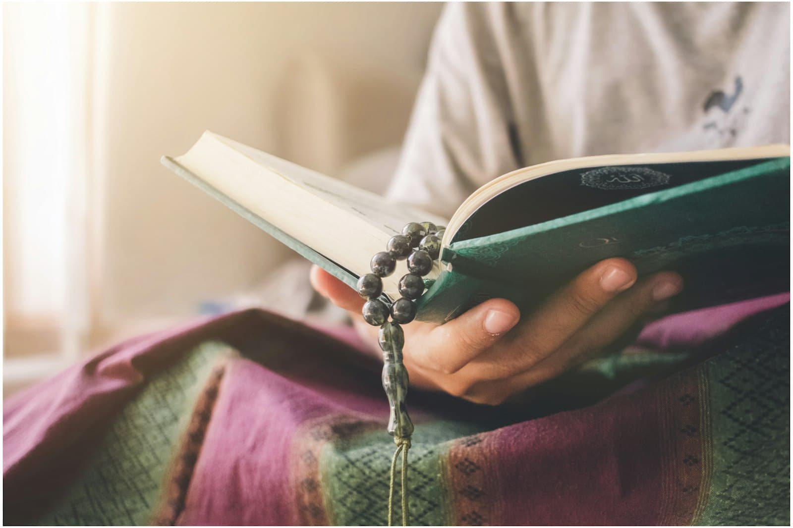 Hands holding an open Quran and prayer beads