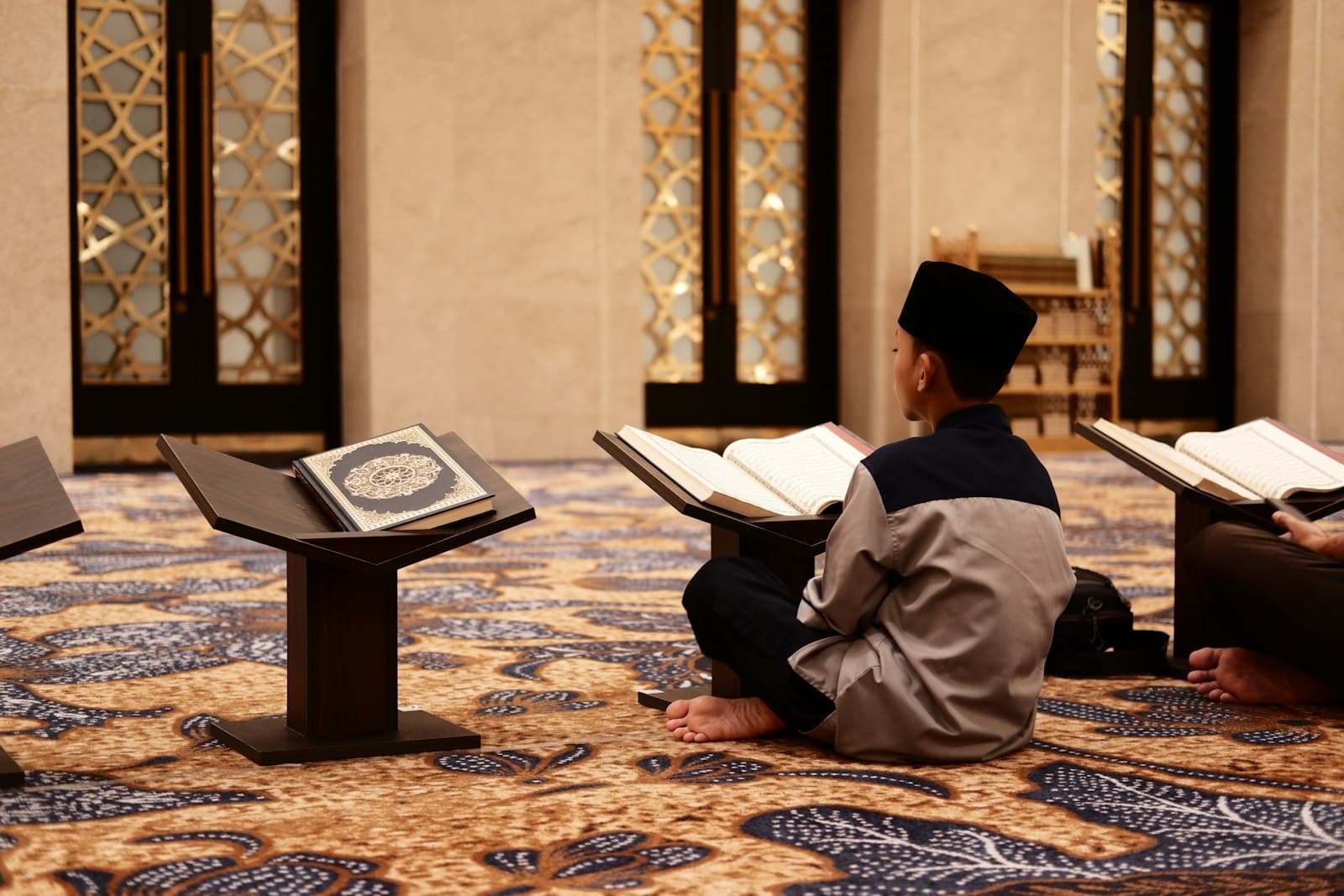 A man sitting on a mosque floor reading the Quran