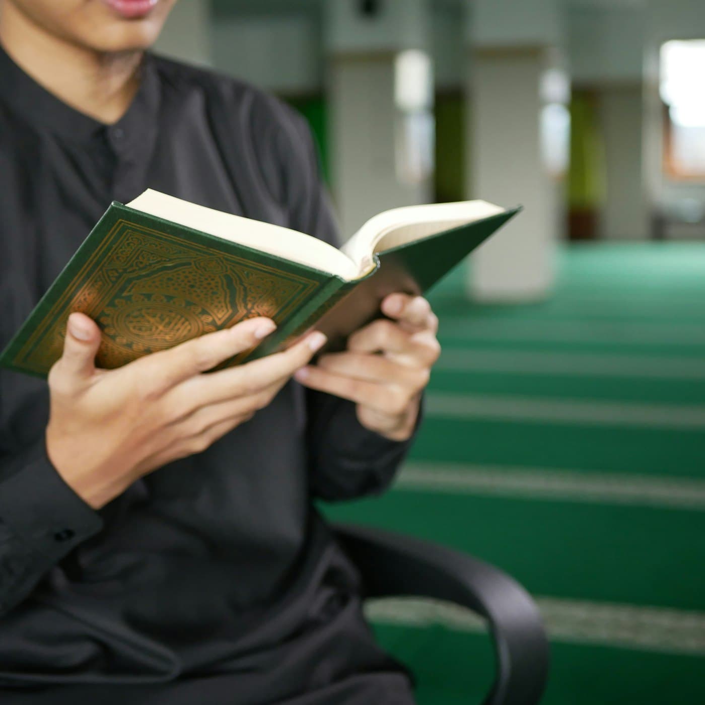 A man reading a green Quran inside a mosque