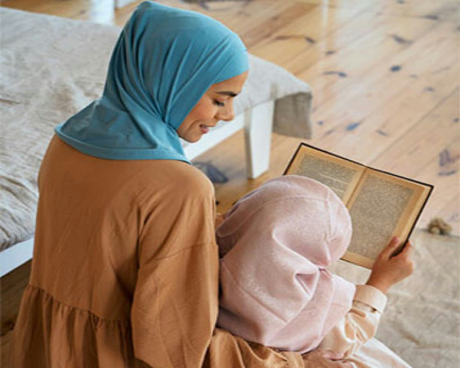 A mother in hijab reading a book with her young daughter