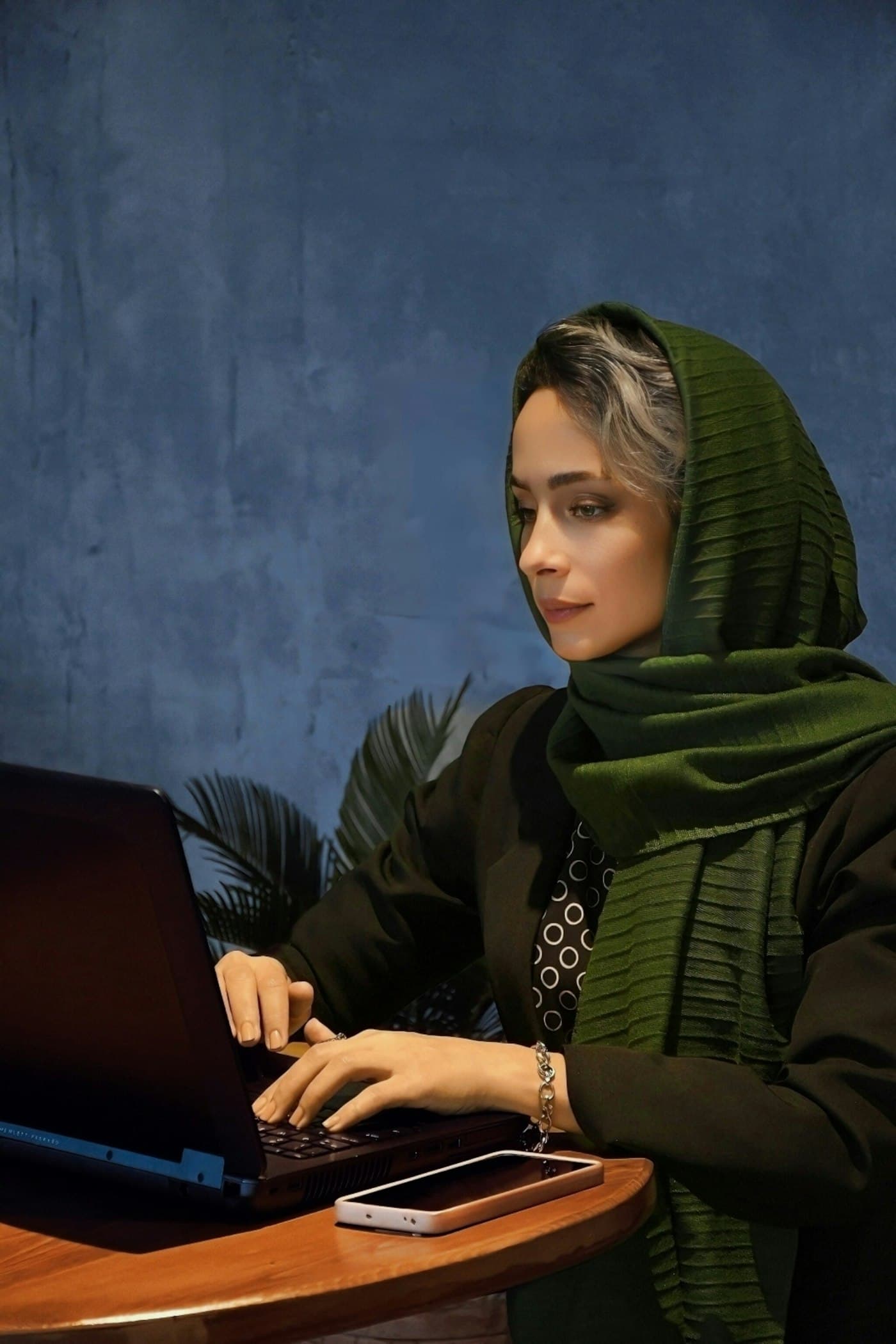 A woman in a green hijab taking an online class on her laptop