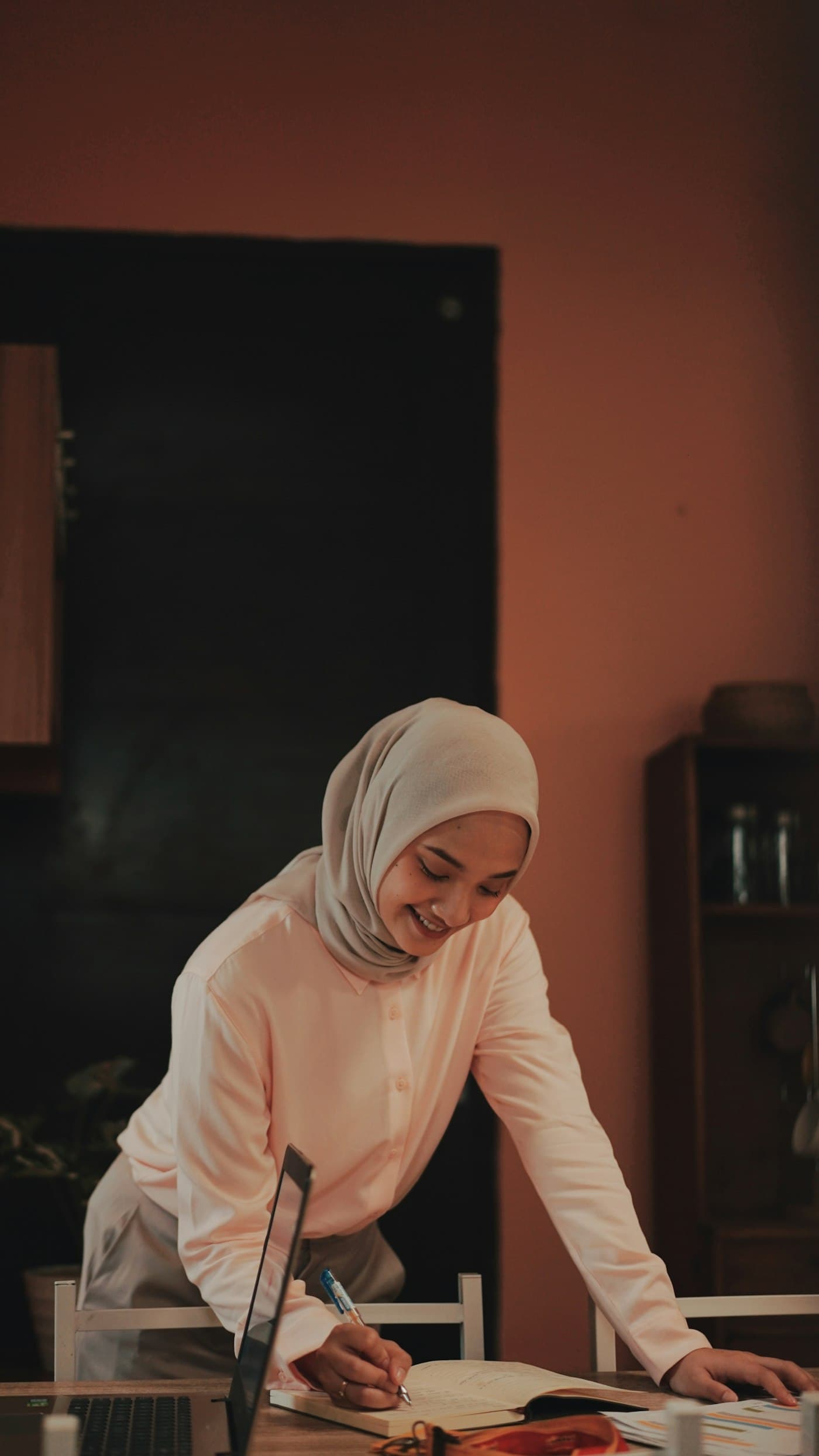 A smiling woman in hijab learning on her laptop at home