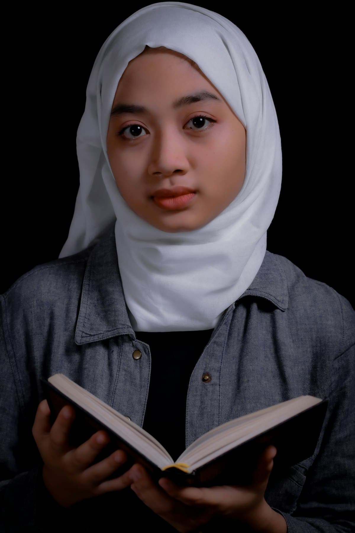 A young woman in a white hijab holding an open book